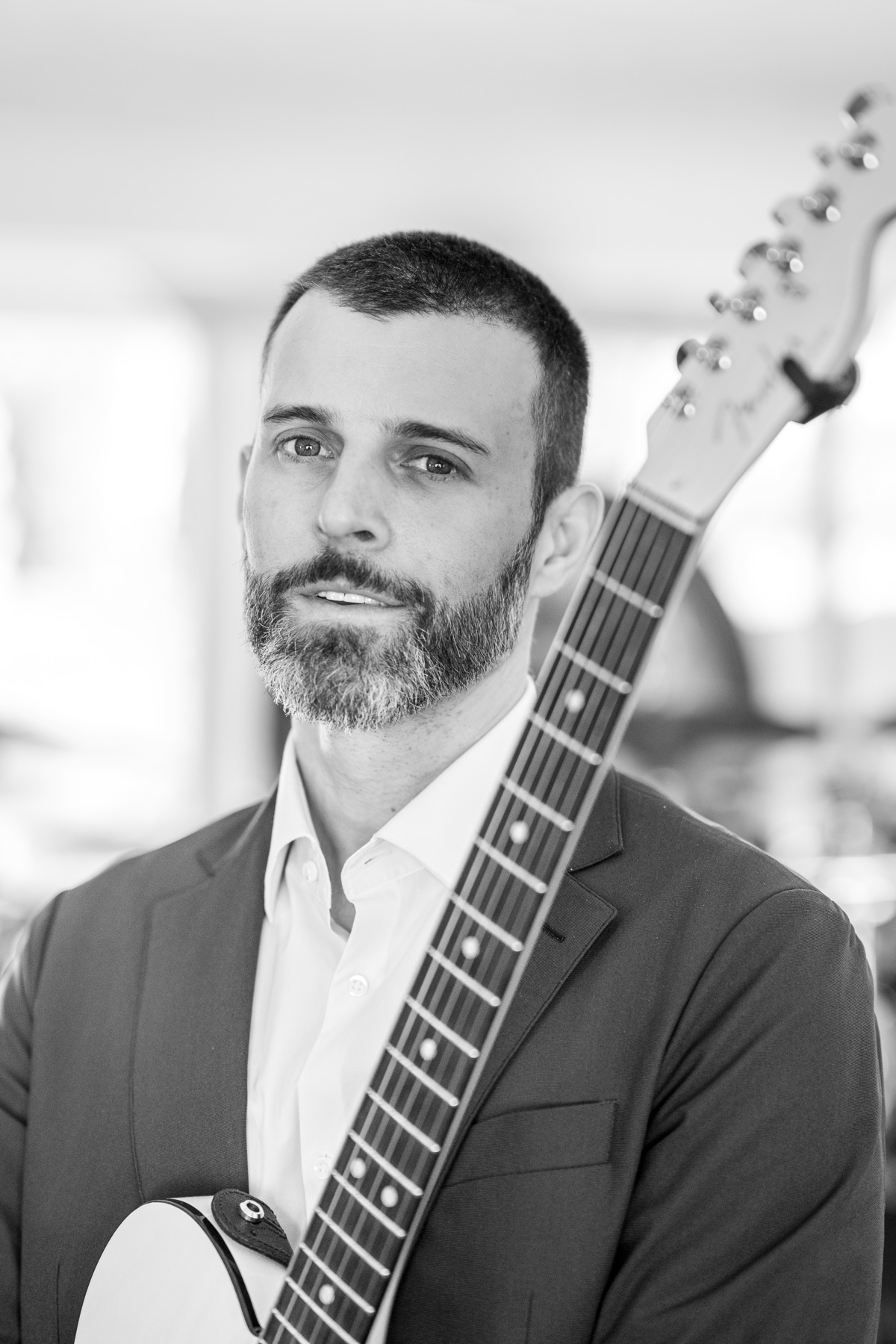Close-up portrait of Coyah Gamble in a suit, guitar neck over his shoulder